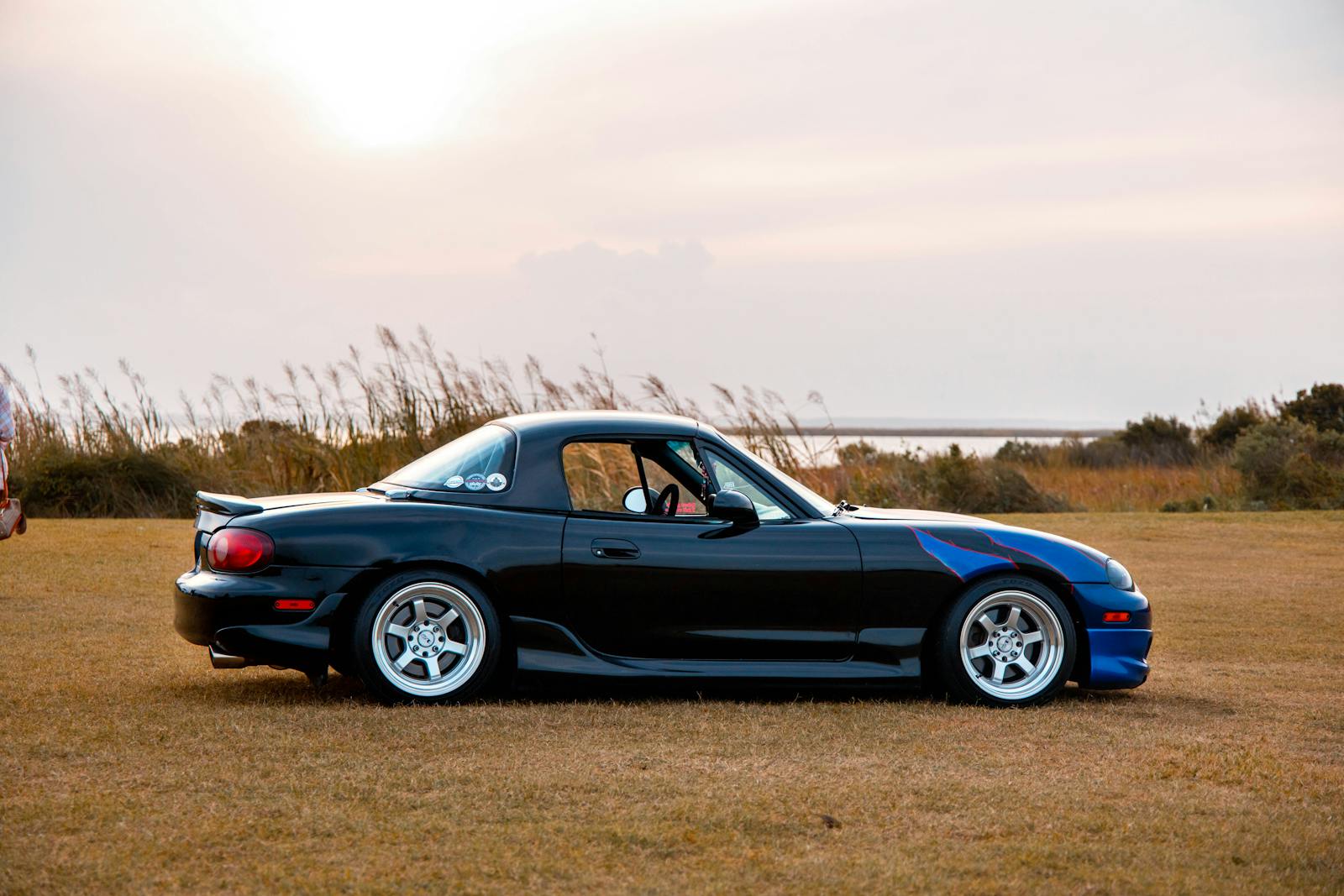 A sleek black sports car parked on a field during sunset, showcasing automotive elegance.